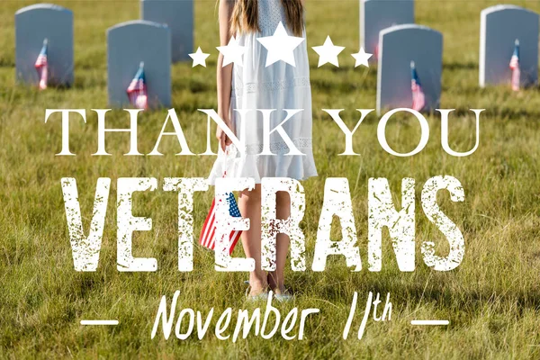 Cropped view of kid in white dress standing on graveyard with american flag with thank you veterans illustration — Stock Photo
