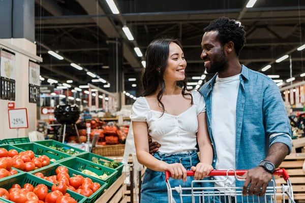 Счастливая межрасовая пара смотрит друг на друга в супермаркете — стоковое фото