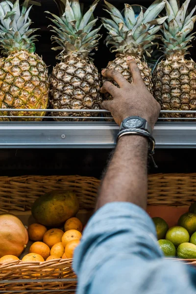 Vista ritagliata dell'uomo africano americano che tocca l'ananas nel supermercato — Foto stock