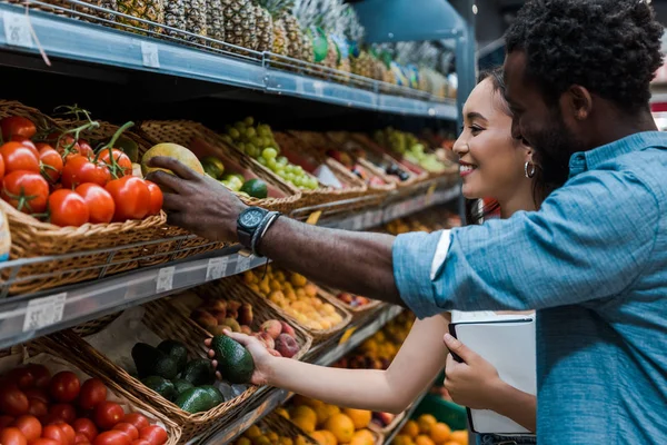 Selective focus of happy asian woman and african american man near tasty fruits in store — Stock Photo