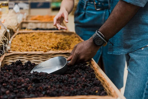 Cropped view of african american man holding metal scoop with raisins near woman gesturing in supermarket — Stock Photo