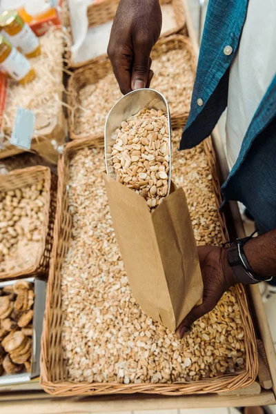 Cropped view of african american man holding metal scoop with tasty peanuts in store — Stock Photo