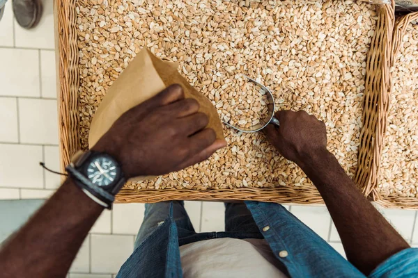Vista superior do homem americano africano que prende a colher do metal com amendoins saborosos perto do saco de papel na loja — Fotografia de Stock