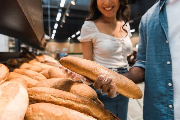 Cropped of african american man holding baguette near happy woman — Stock Photo