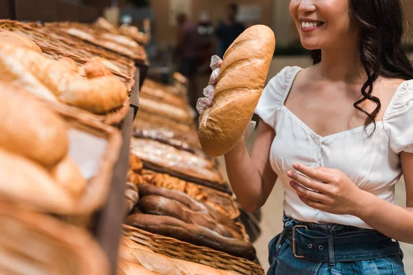 Cropped view of happy woman smiling while smelling bread in supermarket — Stock Photo