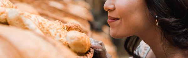 Panoramic shot of cheerful woman smiling while smelling bread in supermarket — Stock Photo