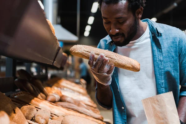 Focalizzazione selettiva dell'uomo afro-americano che odora di pane fresco al supermercato — Foto stock