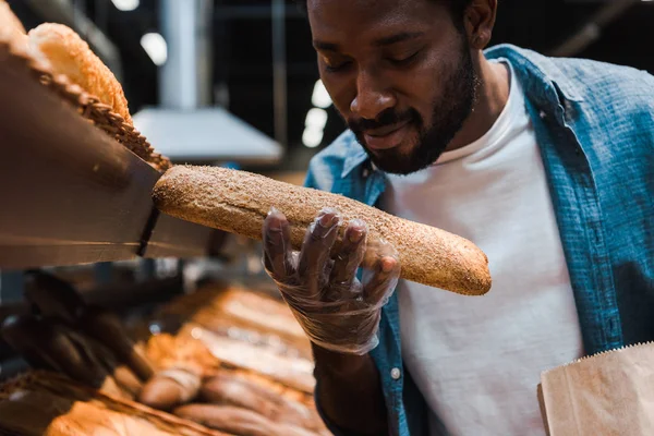 Избирательный фокус счастливого африканского американца, смотрящего на свежий хлеб в супермаркете — стоковое фото