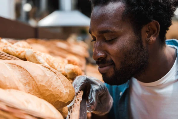 Foco seletivo do homem americano africano feliz cheirando pão fresco no supermercado — Fotografia de Stock