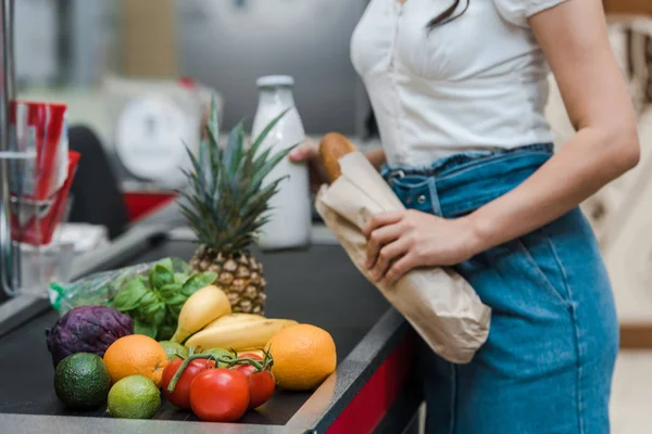 Cropped view of girl holding baguette and glass bottle with milk near supermarket counter — Stock Photo