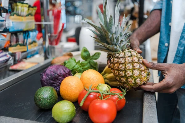 Vista cortada do homem americano africano segurando abacaxi perto de balcão de supermercado com mantimentos — Fotografia de Stock