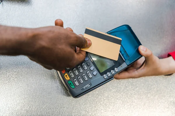 Ausgeschnittene Ansicht eines Afrikaners, der mit Kreditkarte in der Nähe der Kasse im Supermarkt bezahlt — Stockfoto