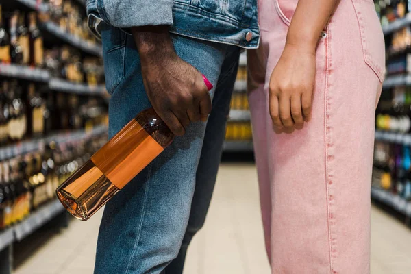 Primo piano dell'uomo afro-americano che tiene in mano la bottiglia con il vino vicino alla donna nel supermercato — Foto stock