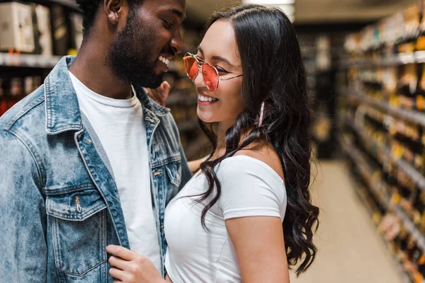 Glücklich afrikanisch-amerikanischer Mann in der Nähe fröhlicher asiatischer Mädchen mit Sonnenbrille — Stockfoto