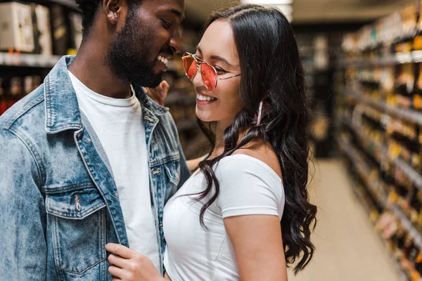 Feliz africano americano hombre cerca alegre asiático chica en gafas de sol — Stock Photo