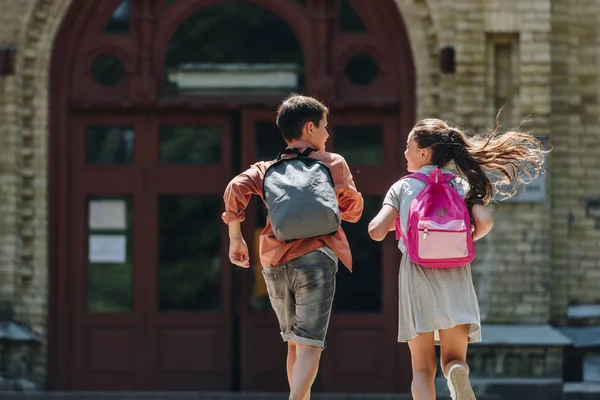 Vue arrière de deux écoliers avec des sacs à dos en cours d'exécution dans la cour d'école — Photo de stock