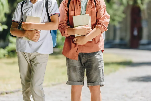 Cropped view of two schoolboys holding books while walking together — Stock Photo