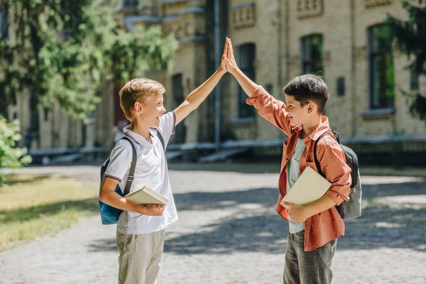 Two cheerful schoolboys giving high five while standing in schoolyard — Stock Photo