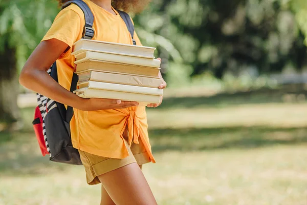 Обрізаний вид афроамериканської школярки з рюкзаком, що тримає книги — стокове фото