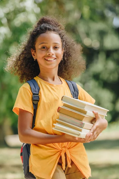 Fröhliche afrikanisch-amerikanische Schülerin hält Bücher in der Hand und lächelt in die Kamera — Stockfoto