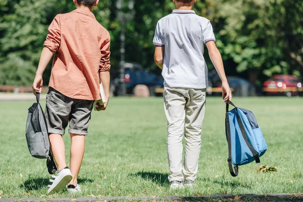 Rückansicht von zwei Schülern mit Rucksäcken, die auf Rasen im Park spazieren — Stockfoto