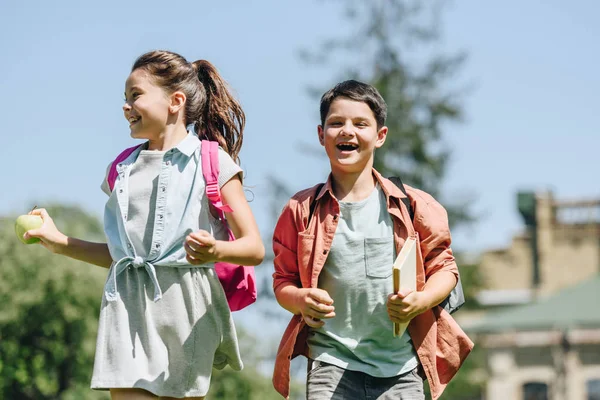 Zwei glückliche Schulkinder mit Rucksäcken lächeln beim Laufen im Park — Stockfoto