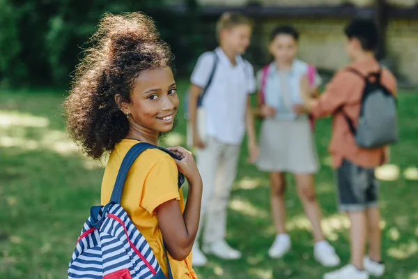 Selective focus of adorable african american schoolgirl smiling at camera near multiethnic friends — Stock Photo