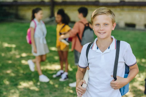 Selective focus of smiling schoolboy looking at camera while standing near multicultural friends — Stock Photo
