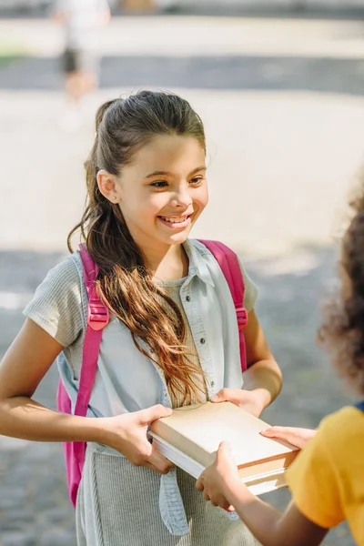 Cropped view of african american schoolgirl giving books to smiling friend — Stock Photo