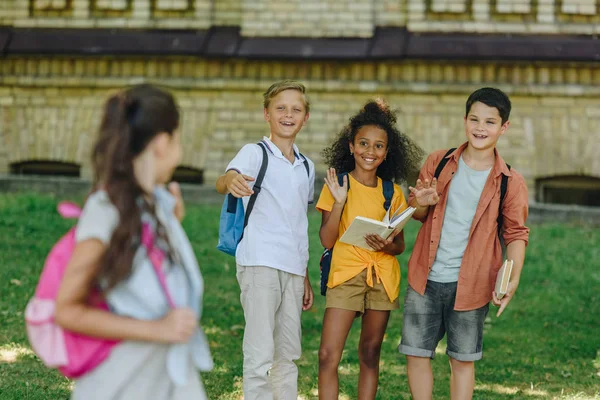 Selective focus of multicultural schoolkids waving hands to schoolgirl — Stock Photo