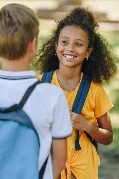 Vue arrière de écolier debout près souriant afro-américaine écolière — Photo de stock