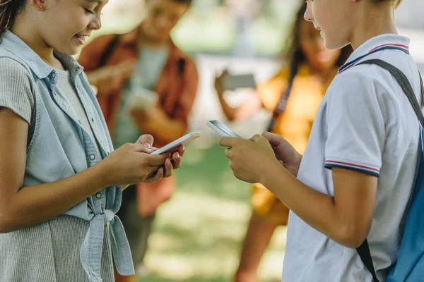 Selektiver Fokus von Schülern, die Smartphones nutzen, während sie in der Nähe multikultureller Freunde stehen — Stockfoto