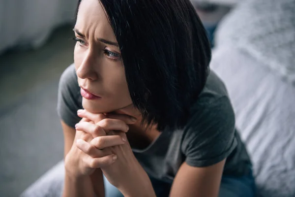 Beautiful depressed woman sitting on bed with clenched hands at home — Stock Photo