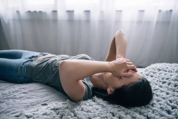 Mujer deprimida acostada en la cama y cubriendo la cara en casa - foto de stock