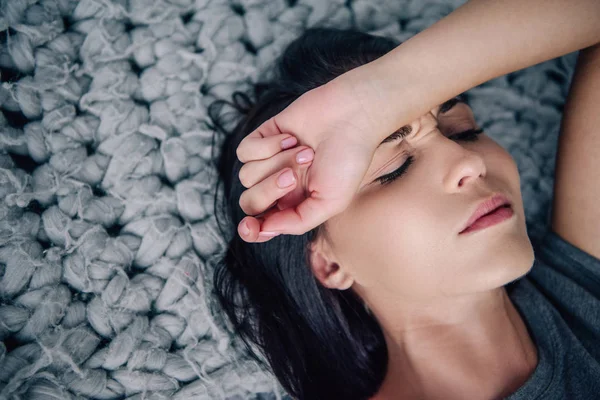 Beautiful depressed woman lying on bed with hand on forehead at home — Stock Photo