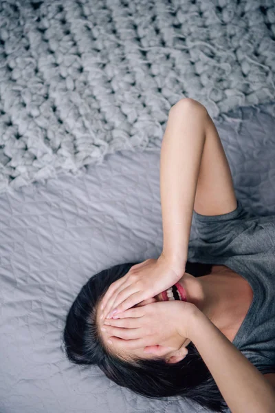 Депрессивная женщина покрывает лицо и плачет, лежа на кровати дома — стоковое фото