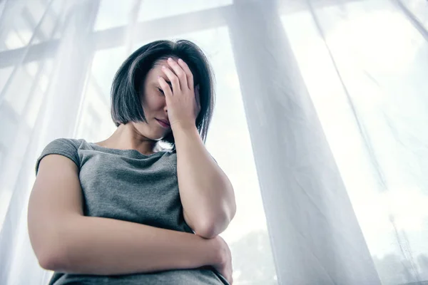 Vista angolo basso della donna depressa che copre il viso a casa — Foto stock