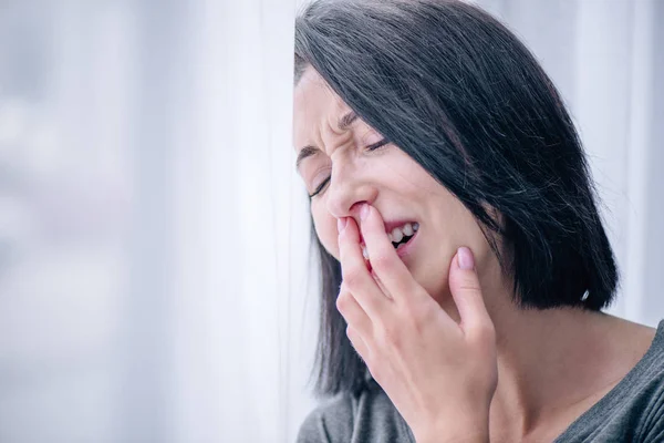 Selective focus of depressed brunette woman covering mouth and crying at home — Stock Photo