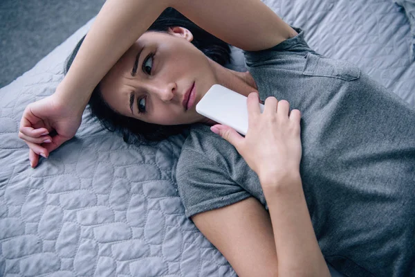 Beautiful lonely depressed woman on bed with smartphone in bedroom — Stock Photo