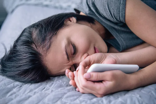 Mujer deprimida solitaria acostada en la cama y sosteniendo el teléfono inteligente en el dormitorio - foto de stock