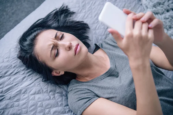 Beautiful depressed woman on bed using smartphone in bedroom — Stock Photo