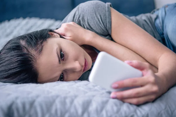 Lonely sad woman on bed using smartphone in bedroom — Stock Photo