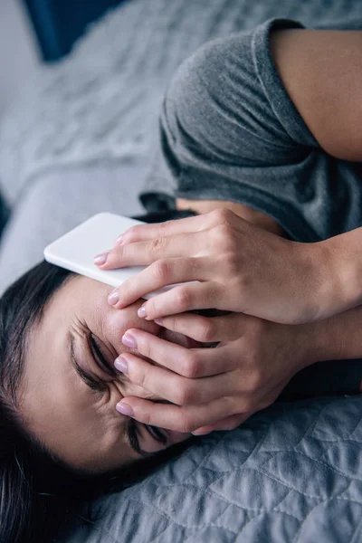 Mujer deprimida solitaria en la cama hablando en el teléfono inteligente y llorando en el dormitorio - foto de stock