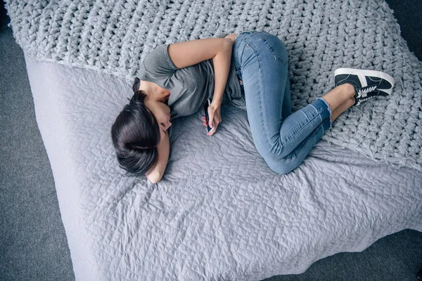 Vista dall'alto della donna depressa solitaria sul letto utilizzando lo smartphone in camera da letto — Foto stock