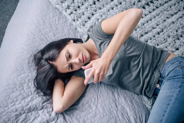 Lonely depressed woman on bed using smartphone in bedroom — Stock Photo