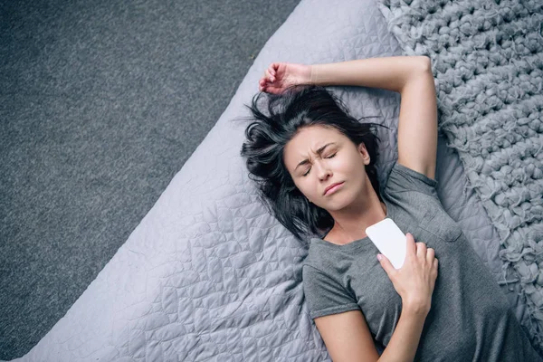 Вид на одинокую депрессивную женщину на кровати со смартфоном в спальне — стоковое фото