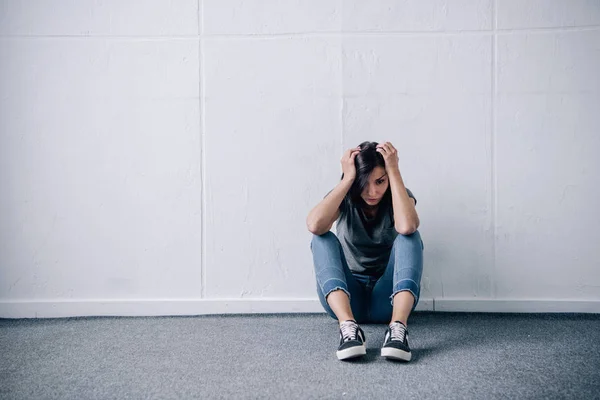 Депрессивная одинокая брюнетка с руками на голове сидит на полу дома — стоковое фото