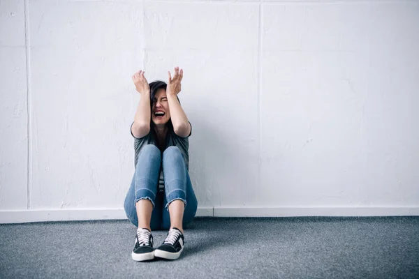 Mujer morena deprimida con las manos en la cabeza sentada y gritando en casa - foto de stock