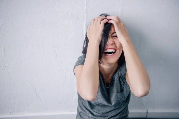 Molesto mujer morena solitaria cubriendo la cara y gritando en casa - foto de stock