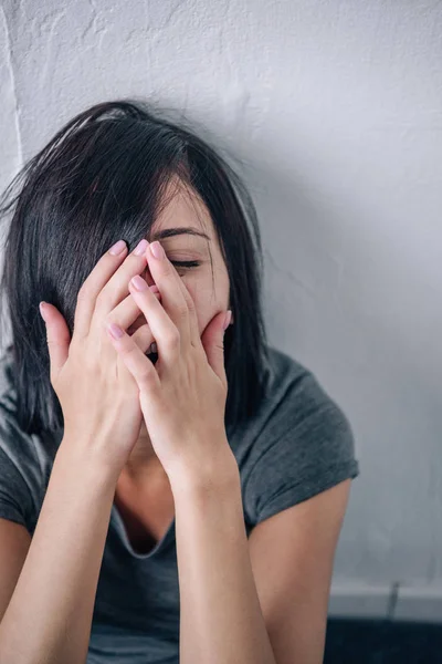 Molesto mujer morena solitaria llorando y cubriendo la cara en casa con espacio de copia - foto de stock